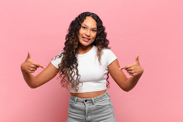 young hispanic woman looking proud, arrogant, happy, surprised and satisfied, pointing to self,...