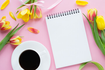 Notebook, cup of coffee, colorful tulips on pink background