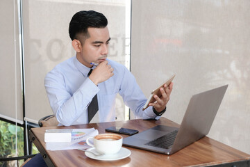 Young asian business man working with laptop, tablet and papers on desk at office.