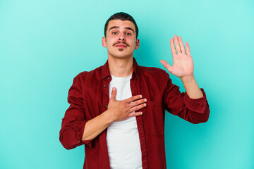Young caucasian man isolated on blue background taking an oath, putting hand on chest.