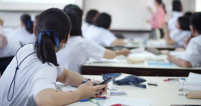 An Asian female student in a white school uniform and wearing a mask to prevent covid-19, sitting in study group using a calculator to solve problems by teachers with a projector.