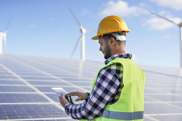 Young man working at solar power station with digital tablet - Renewable energry with wind turbines...