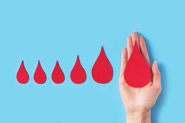 World hemophilia day concept with red blood drop simbol and hands on blue background