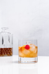 Vaso de vermut con hielo decorado con una rodaja de naranja y cereza sobre mesa blanca 