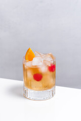 Vaso de vermut con hielo decorado con cerezas y rodajas de naranja sobre mesa blanca