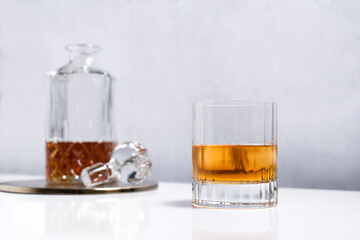 Vaso de brandy con hielo y decantador abierto sobre mesa blanca
