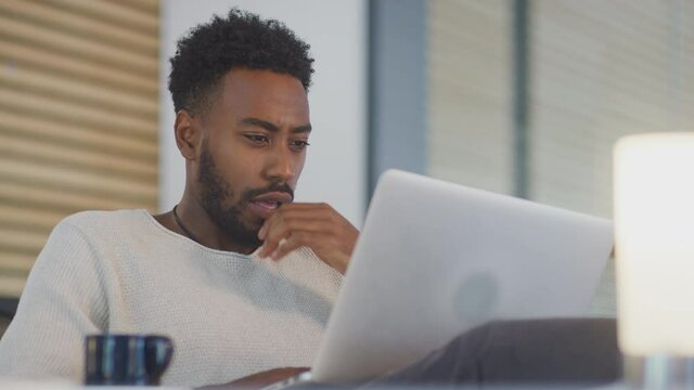 Young businessman working late sitting at desk with laptop in modern open plan office - shot in slow motion