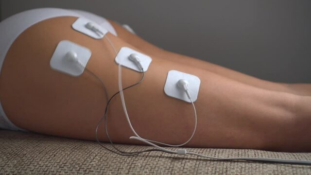 Electrical-stimulation TENs of the girl's buttocks and legs with vibration impulses from the electrodes.