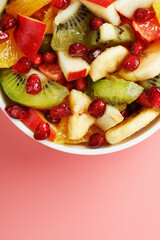 Salad of different juicy ripe fruits in a white cup on a pink background.