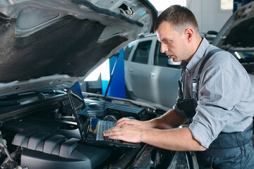 car mechanic using a computer laptop to diagnosing and checking up on car engines parts for fixing...