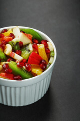 Fruit salad in a white cup on a black background, free space for text.