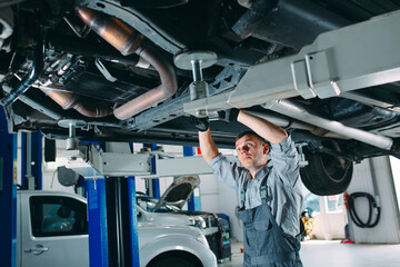 Portrait of a mechanic repairing a lifted car.