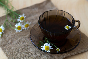 dark glass cup of Herbal tea with chamomile tea on sackcloth on a light wooden table with copy...