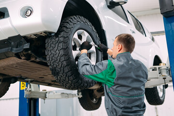 Car lifted in automobile service for fixing, worker repairs the wheel,