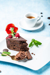 Delicious chocolate cake in white plate with a cup of coffee on a blue background, vertical image, place for text