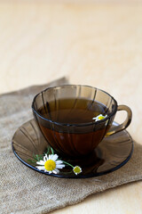hot glass cup of Herbal tea with chamomile tea on sackcloth on a light wooden table with copy space. cup fo tea with fresh flowers and green leaves on yellow background.vertical