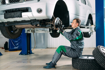 Car lifted in automobile service for fixing, worker repairs the wheel,