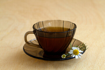 dark glass cup of Herbal tea with chamomile tea on a light wooden table with copy space. cup fo tea...