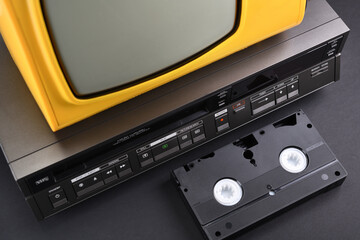 Old yellow vintage TV with VCR and videotape on black background from 1980s, 1990s, 2000s. Stack.
