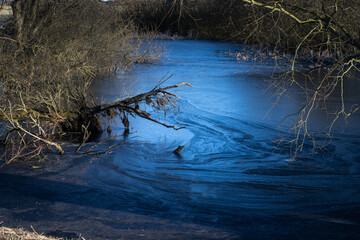 A beautiful picture of a small pond covered with ice. Blue icy water with trees in the background