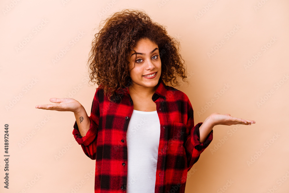 Wall mural young african american woman isolated on beige background confused and doubtful shrugging shoulders 