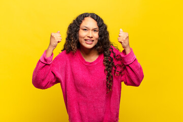 young hispanic woman feeling happy, positive and successful, celebrating victory, achievements or...
