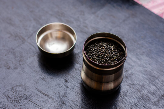 A steel jar full of black lintel or kali dal on a black wooden table.
