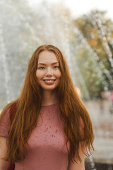 Young beautiful red-haired long-haired woman in a summer pink dress walks through the streets of a summer city.