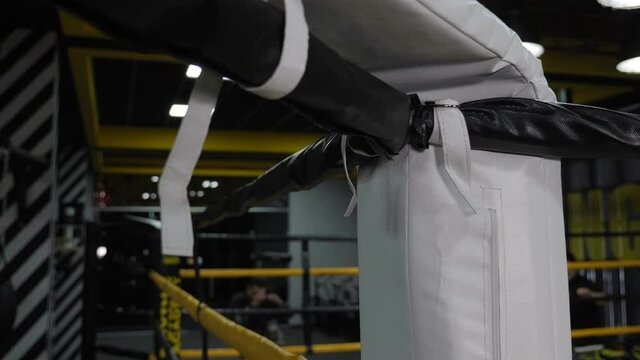 Close-up of a corner of a boxing ring, with a male boxer training in the background.