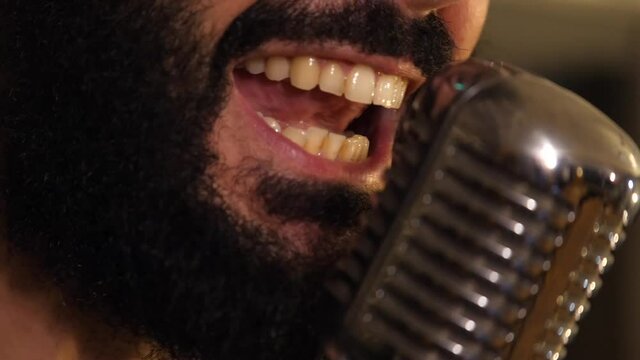 Close-up of a singer with his mouth on the microphone
Man with black beard singing with an old microphone