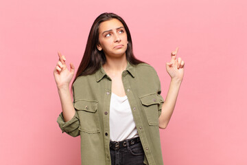 young pretty woman crossing fingers anxiously and hoping for good luck with a worried look