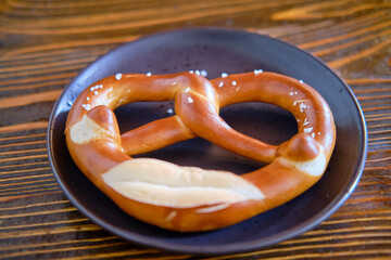 Brezel lies in a plate on a wooden table in a cafe, close-up