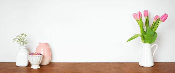 Home decor on a shelf. Vases, flowers and succulent plant. Wood shelf against a white wall. Banner with copy space.