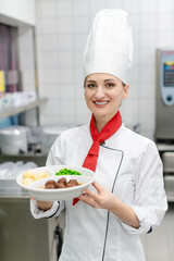 Cook showing plate with food in commercial kitchen of canteen