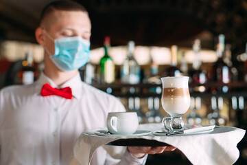 A European-looking waiter in a medical mask serves Latte coffee.