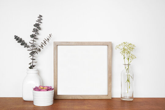 Mock up square wood frame with home decor.  Succulent, eucalyptus branches and flowers. Wooden shelf against a white wall. Copy space.