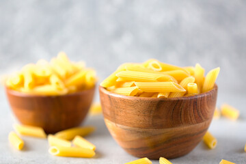 Uncooked yellow pasta in a wooden bowl on gray table. Selective focus. Italian food concept. Copy space. World Pasta Day.