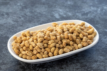 Dry mulberry on plate on dark background