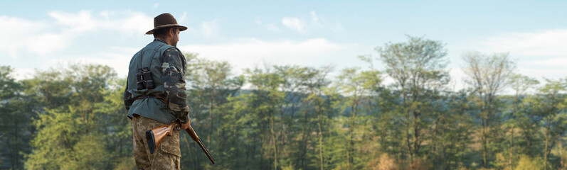 A hunter with a gun in his hands in hunting clothes in the autumn forest in search of a trophy. A man stands with weapons and hunting dogs tracking down the game.