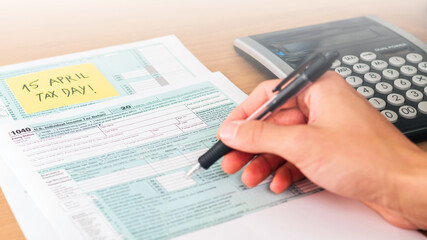 Filling 1040 form on tax day with calculator on table to be returned. American event.