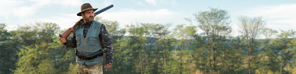 A hunter with a gun in his hands in hunting clothes in the autumn forest in search of a trophy. A...