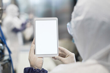 Back view close up of unrecognizable worker holding tablet with blank white screen at modern chemical plant, copy space