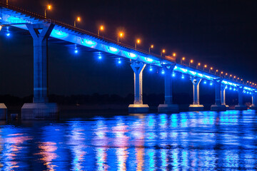 Side view of colourful bridge illuminated with blue color lights at the night. Bridge stands on Volga river in Russia. Blue light is reflected in the water.