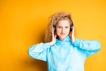 Adorable young girl teenager with curly hair listens to music in the headbands pressing them with her hands