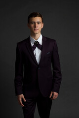 a dark-haired young man in white shirt, dark purple suit and a ribbon male cross bow tie