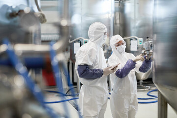 Side view portrait of two workers wearing protective suits while using equipment at modern chemical...