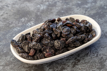 Big black raisins on plate on dark background