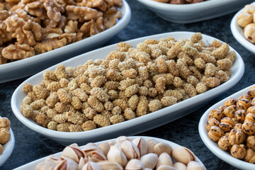 Dry Mulberry in selective focus. Nuts on plate on a dark background. Walnut, Chickpeas, White Chickpeas, Dry mulberry, almond, cashew, pistachio. Types of nuts on the plate.