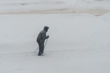 Old man walks in snowstorm practicing nordic poles walking in winter