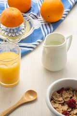 Aerial view of cereal bowl, spoon, oranges, juicer, cloth, jug with milk and glass with orange juice, on white wood, vertical